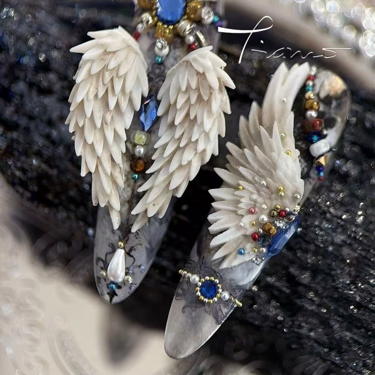 Decorative shoes with angel wings and gemstones on a textured surface