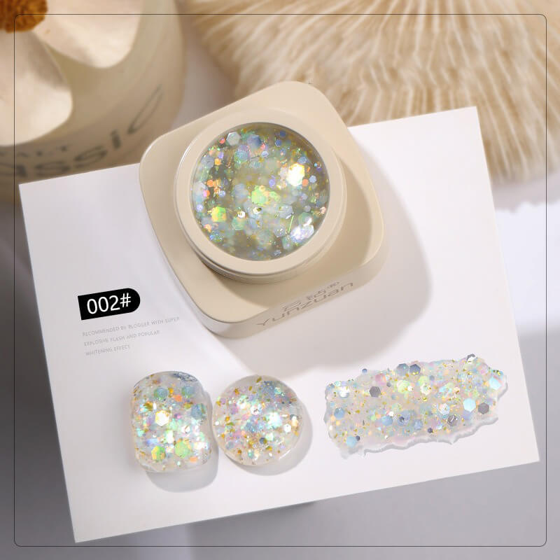 Glittery nail art powder in a container with samples on a white surface