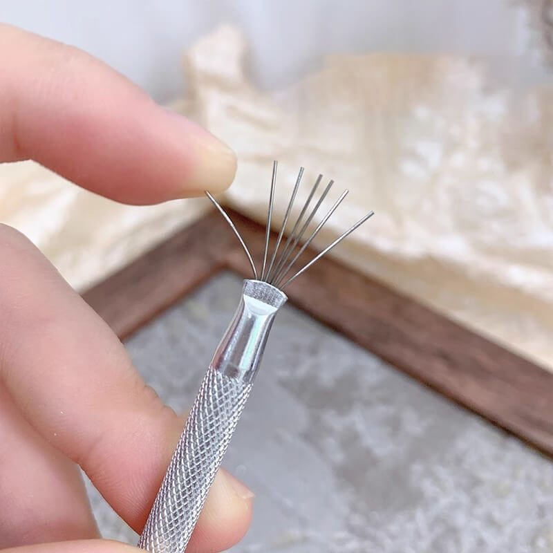 A hand holding a multifunction 7 needle nail art wire pen with metal needles.