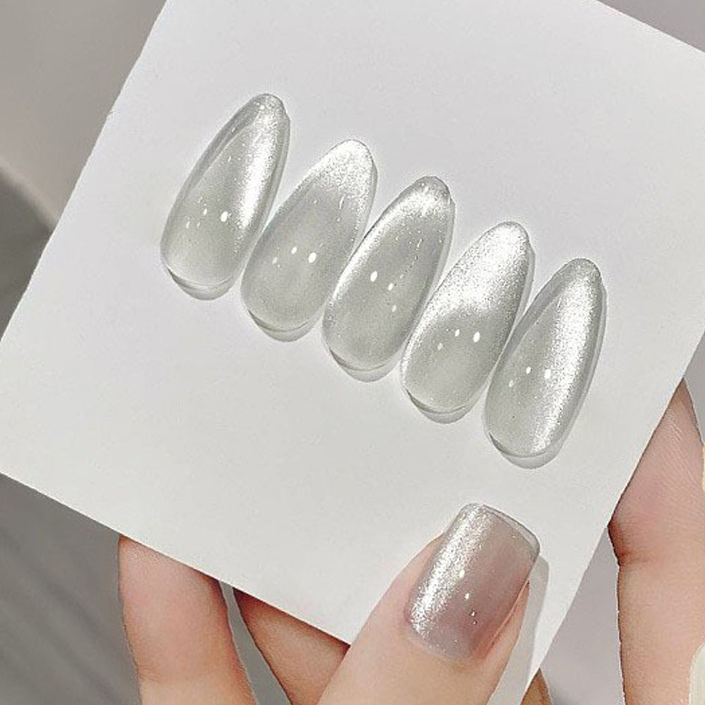 A bottle of cat eye gel nail polish with glitter, placed on a white surface, with a hand holding one of the polish drops, showing a magnetic property.