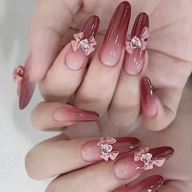 A set of fingernails adorned with pink and red nail polish and decorated with bowknot nail ornaments and rhinestone accessories.