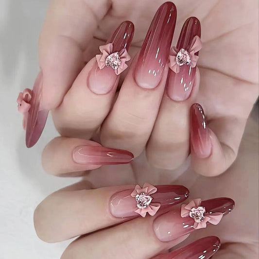 A set of fingernails adorned with pink and red nail polish and decorated with bowknot nail ornaments and rhinestone accessories.