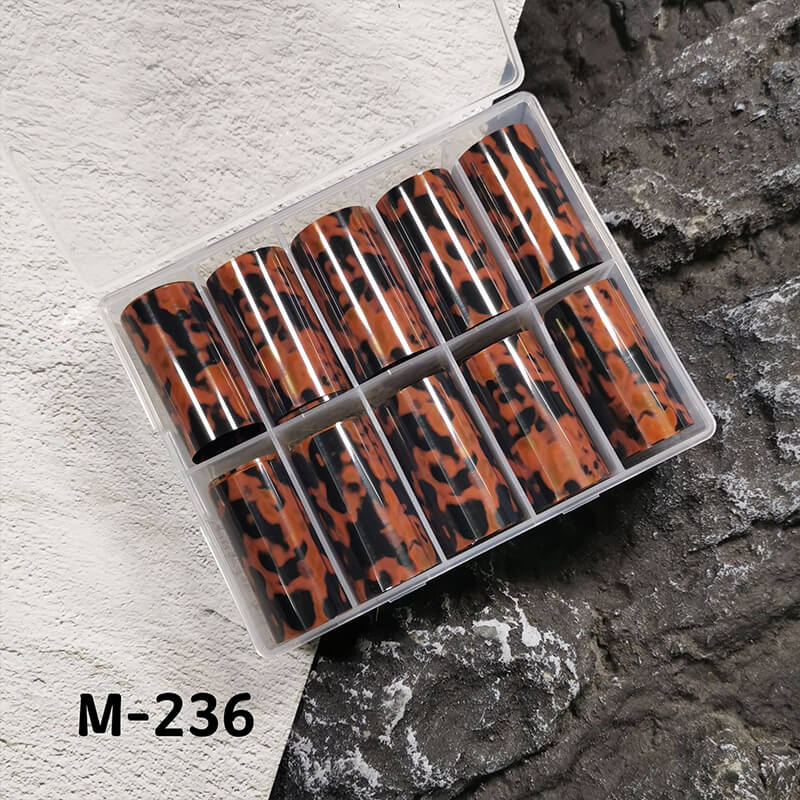 Set of amber pattern nail foils in a clear plastic case on a textured surface.