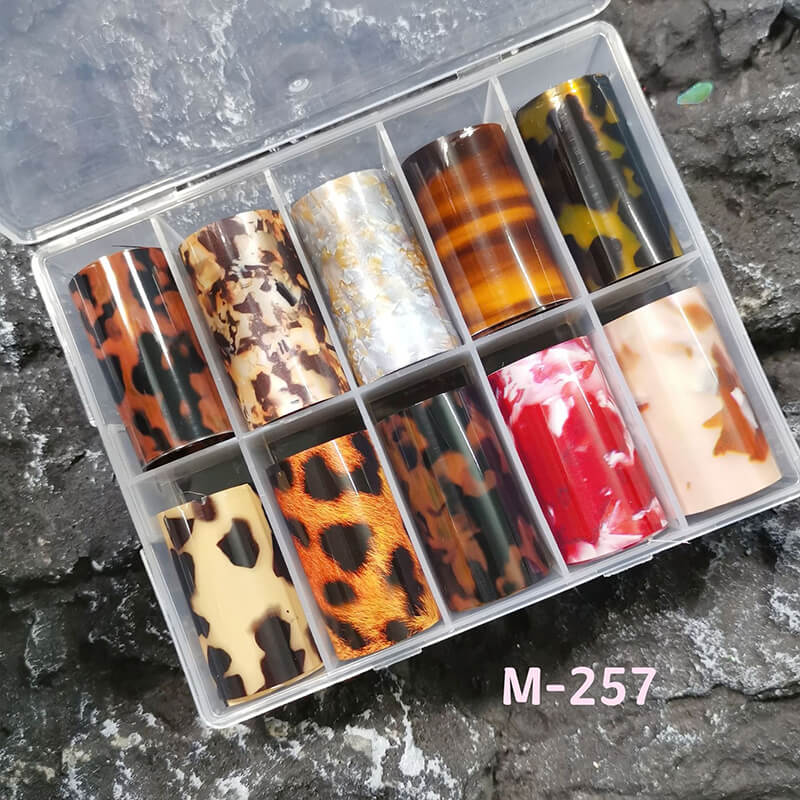 Set of leopard print and other patterned nail foils in a clear plastic case on a stone surface.
