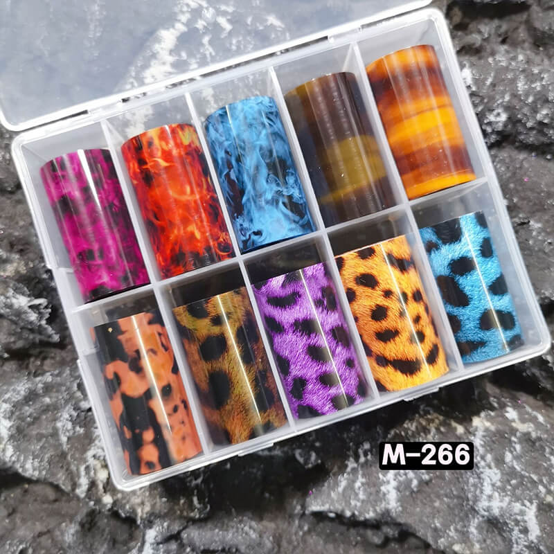 Set of colorful patterned nail foils in a clear plastic case on a rocky surface.