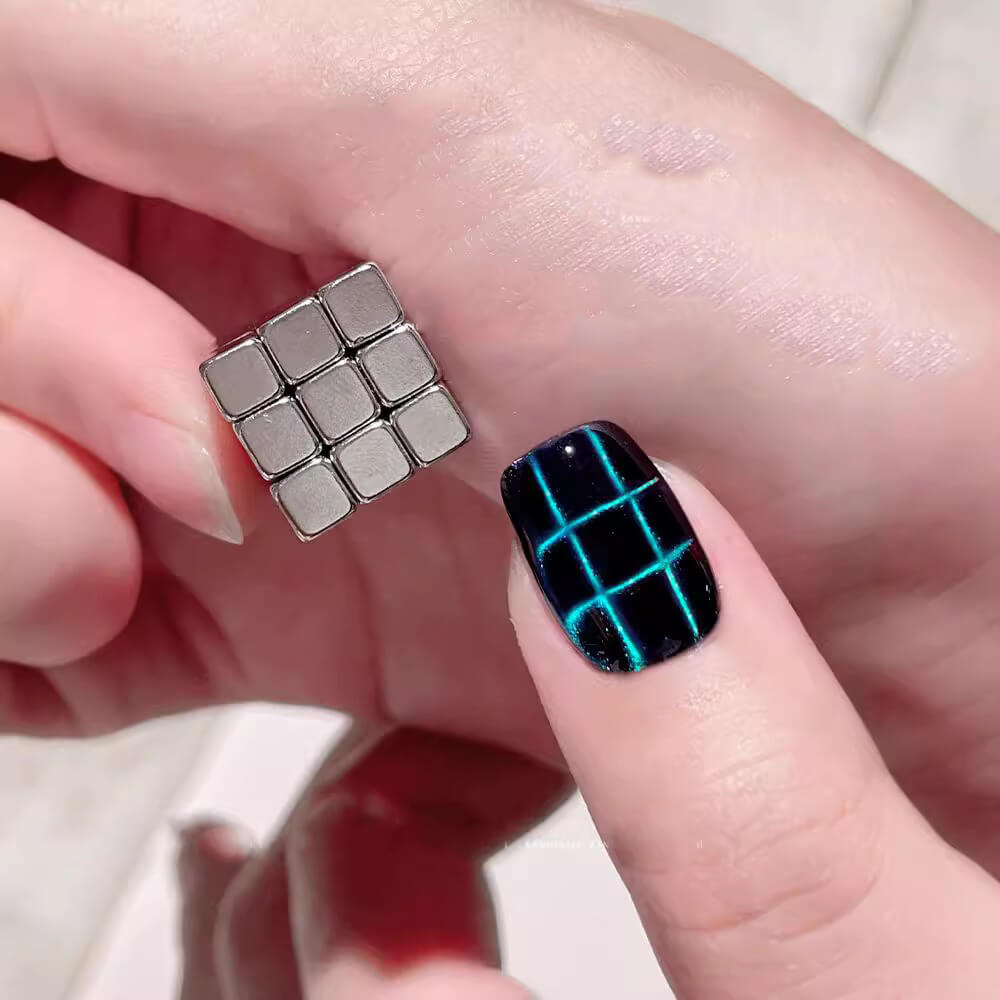 A close-up of a hand holding a 3x3 square magnetic tile next to a fingernail decorated with a black and neon blue grid pattern.