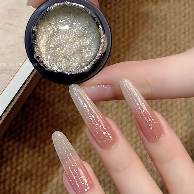Hand with glittery nail polish holding a container of glitter.