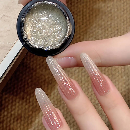 Hand with glittery nail polish holding a container of glitter.