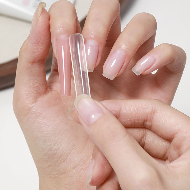 Hand holding a clear nail extension over another hand with natural nails.