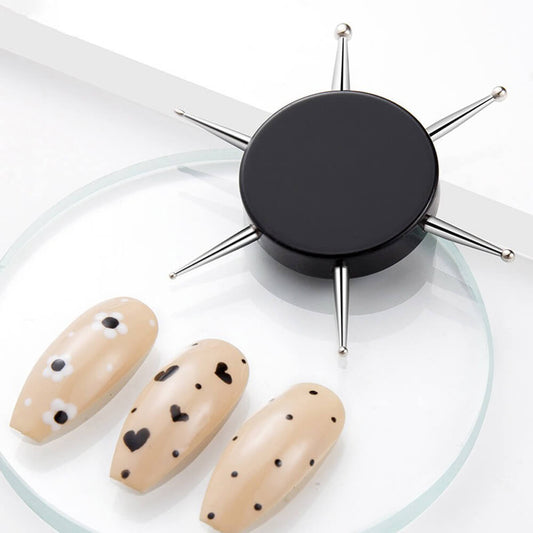 A set of nail art dotting tools with multiple needle-like attachments and a central dotting pen, displayed alongside a set of faux nails with dotted patterns.