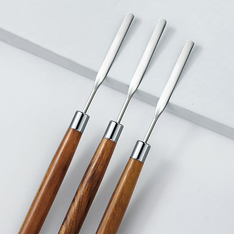 Three nail art mix tools with wooden handles and metal ends, lying on a white surface.