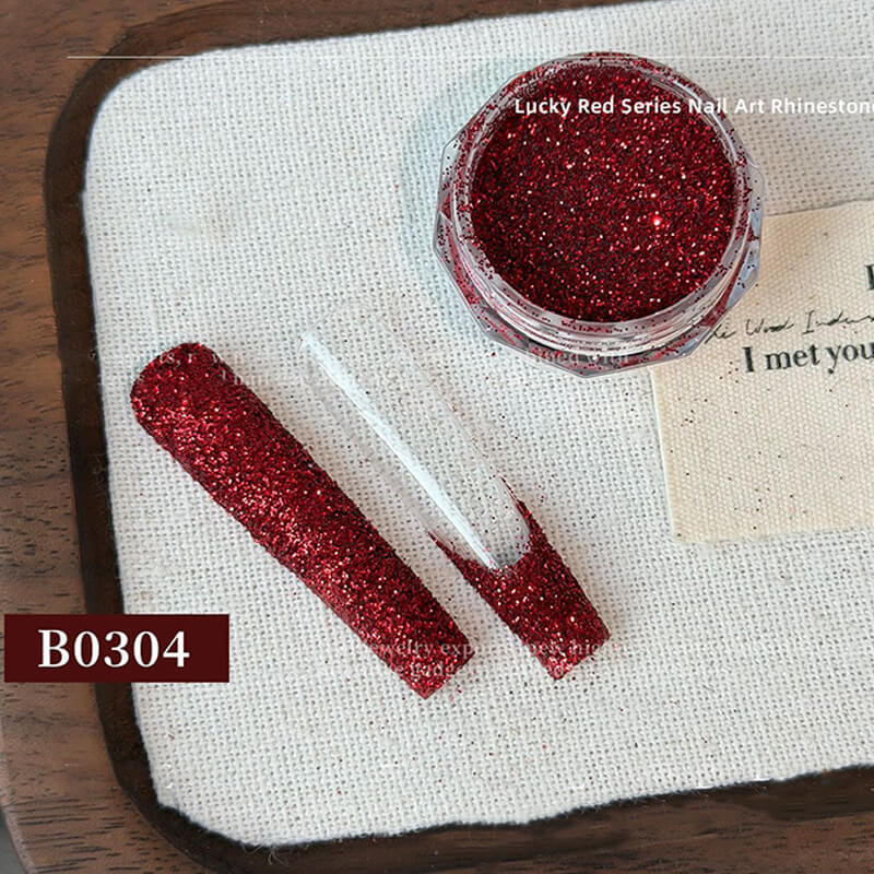 Red glittery nail art rhinestones with container and applicator on a textured surface