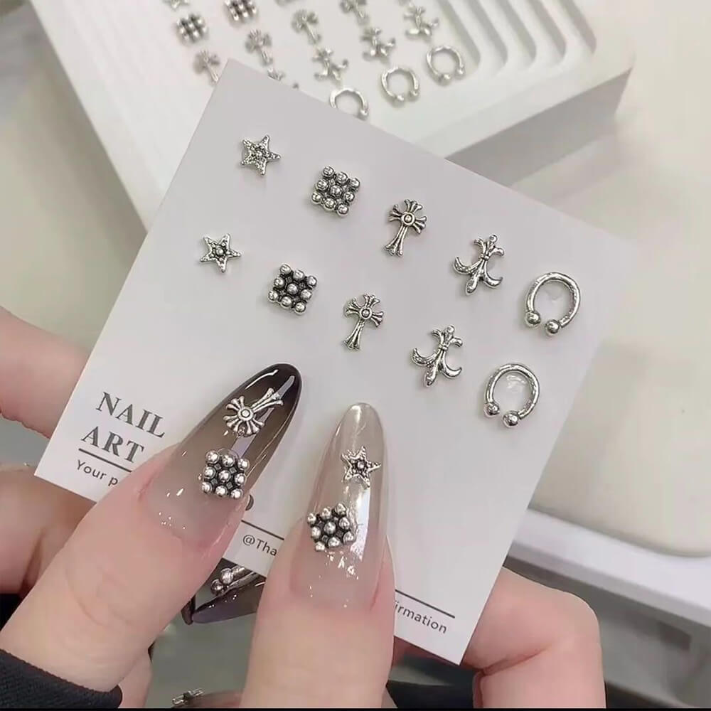 A collection of silver-colored alloy nail charms with various designs displayed on a card, held by a person showcasing the nails.