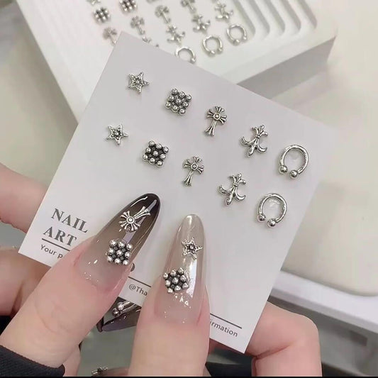 A collection of silver-colored alloy nail charms with various designs displayed on a card, held by a person showcasing the nails.