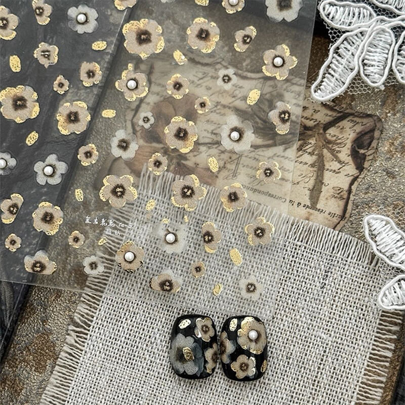 Single vintage black and gold floral sticker showing intricate embossed petal texture.