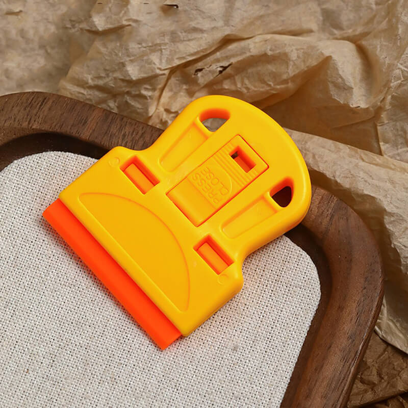 Yellow and orange plastic nail scraper on a textured surface with brown paper in the background
