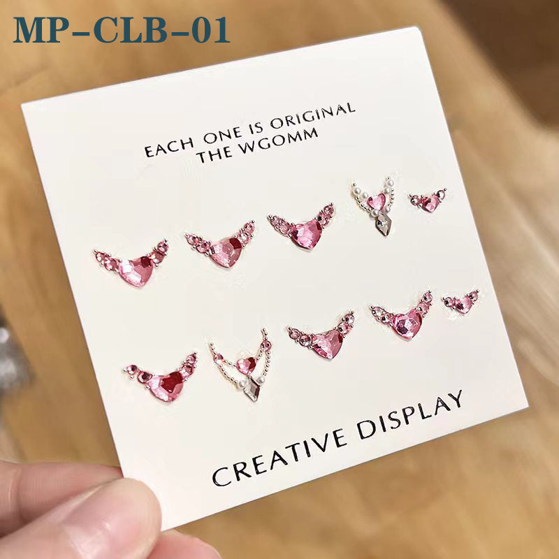 A package of heart-shaped rhinestone decorations for nails, with various shades of pink and red, held in a hand.