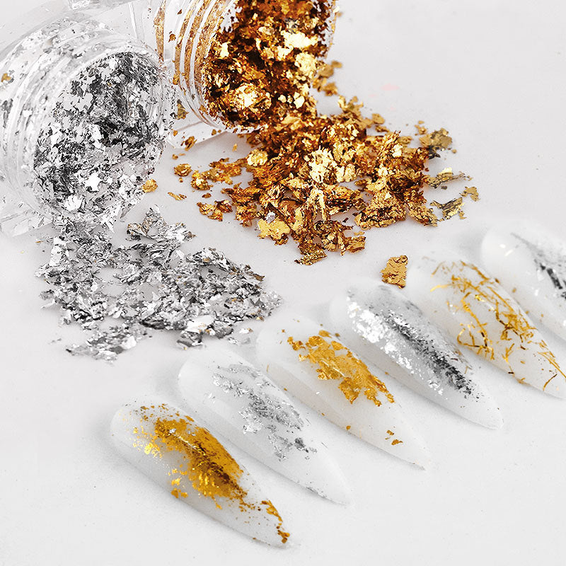 A variety of gold and silver nail decorations and DIY tools spread out on a white surface.
