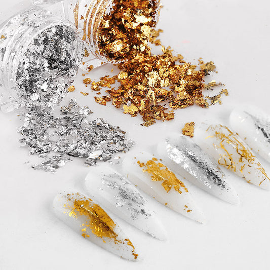A variety of gold and silver nail decorations and DIY tools spread out on a white surface.