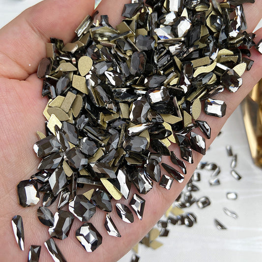 A hand holding a collection of glittery rhinestone nail art jewelry flat back diamond gems.