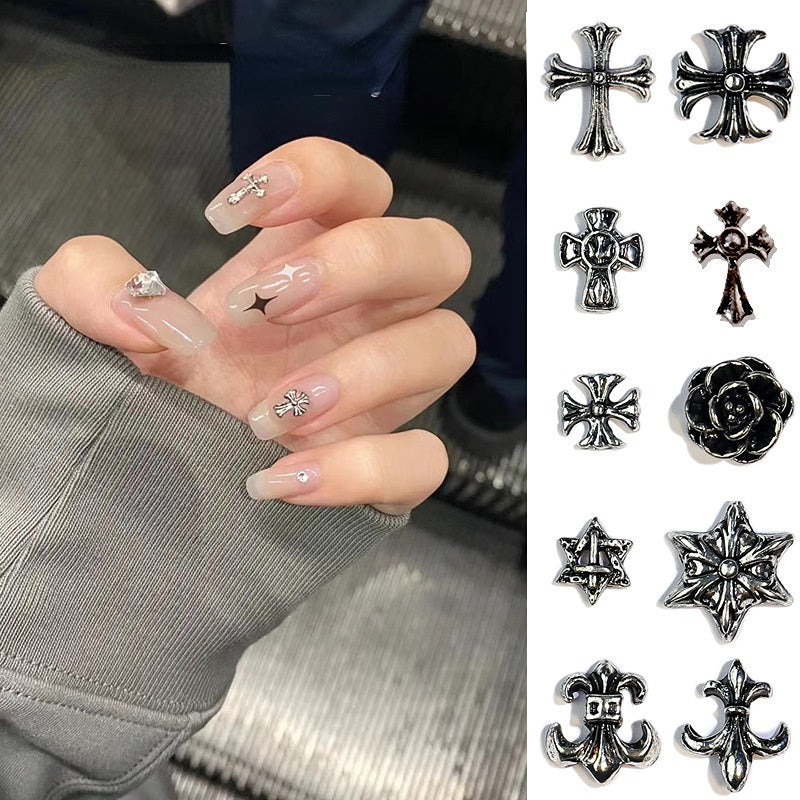 A collection of nail art charms in various designs including crosses and hearts, applied to fingernails and displayed separately against a grey background.