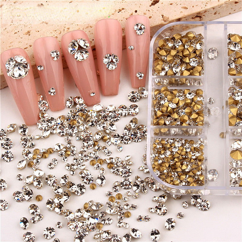 A variety of transparent and colored rhinestones for nail art, placed on a clear plastic surface with some rhinestones scattered beside a set of nails they are used for decoration.