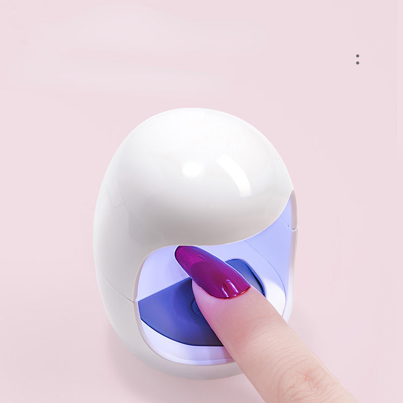 Compact white and blue mini LED nail lamp with a finger pressed against it, indicating use for nail drying.
